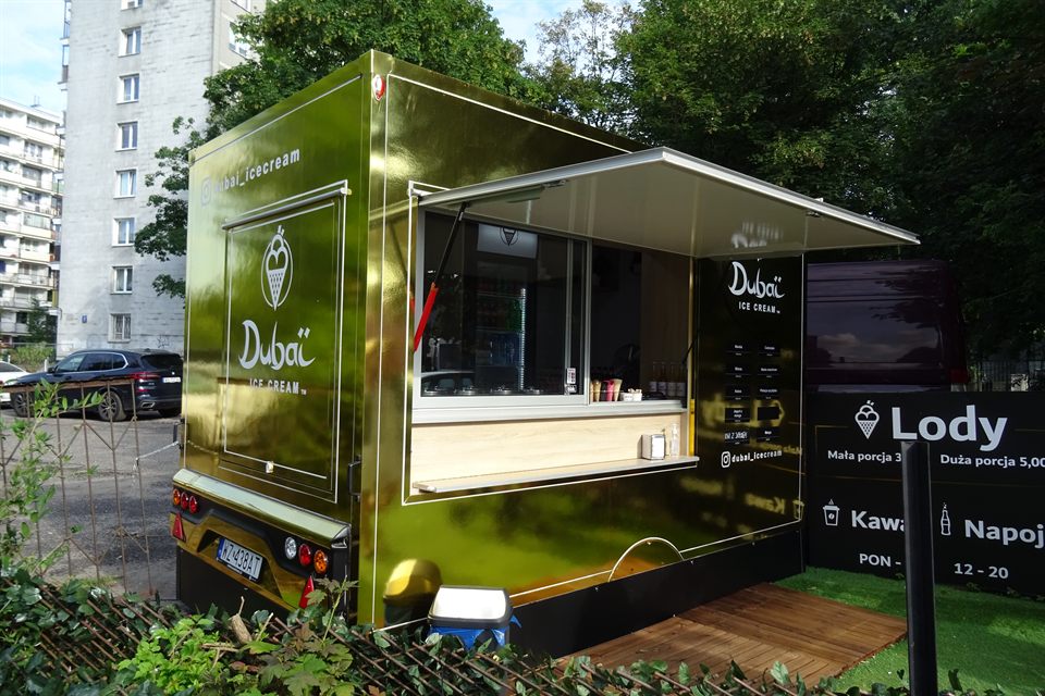Złota przyczepa gastronomiczna Dubai Ice Cream z oknem sprzedażowym na placu miejskim